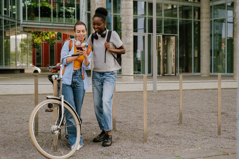 Jovens mulheres multirraciais sorrindo e usando celular na rua da cidade imagem de stock royalty free