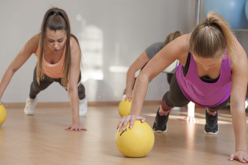 Sporty young women training with medicine balls in fitness class. Group exercise in modern fitness center. Sporty young women training with medicine balls in fitness class. Group exercise in modern fitness center.