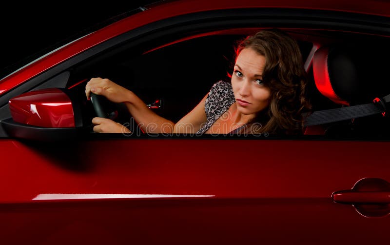 A beautiful young woman caught making a turn in a red sports car at night with the reflection of a red light she could possibly be running in the car. A beautiful young woman caught making a turn in a red sports car at night with the reflection of a red light she could possibly be running in the car.