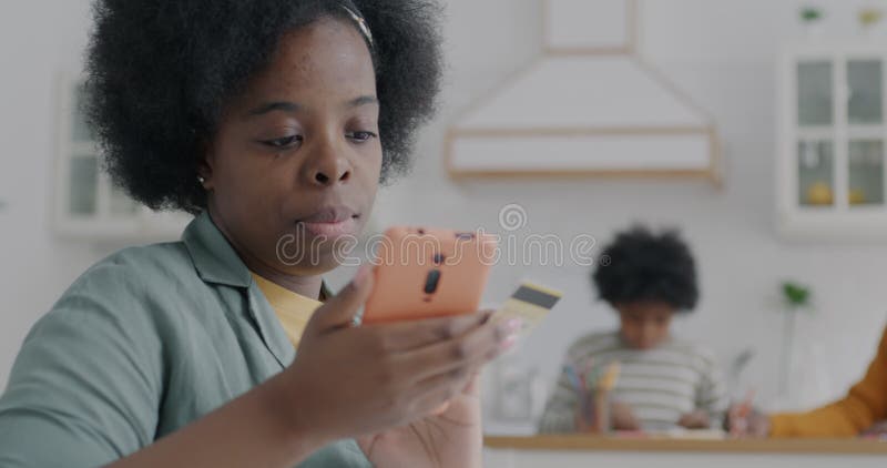 Joyeuse afro-américaine jeune mère acheter en ligne avec carte de crédit et smartphone pendant que enfant et homme visible dans banque de vidéos