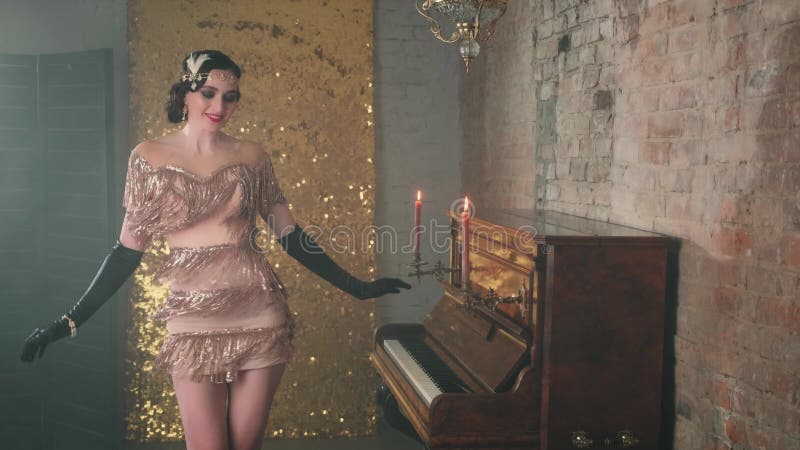 Joyeuse belle jeune femme dans brillante robe dorée de luxe sourires robe gown flutant danses dans la chambre près du piano banque de vidéos