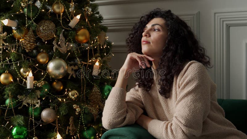 Joyeuse femme aux cheveux crépus, assise près de l'arbre de noël, regardant au loin en faisant un voeu clips vidéos