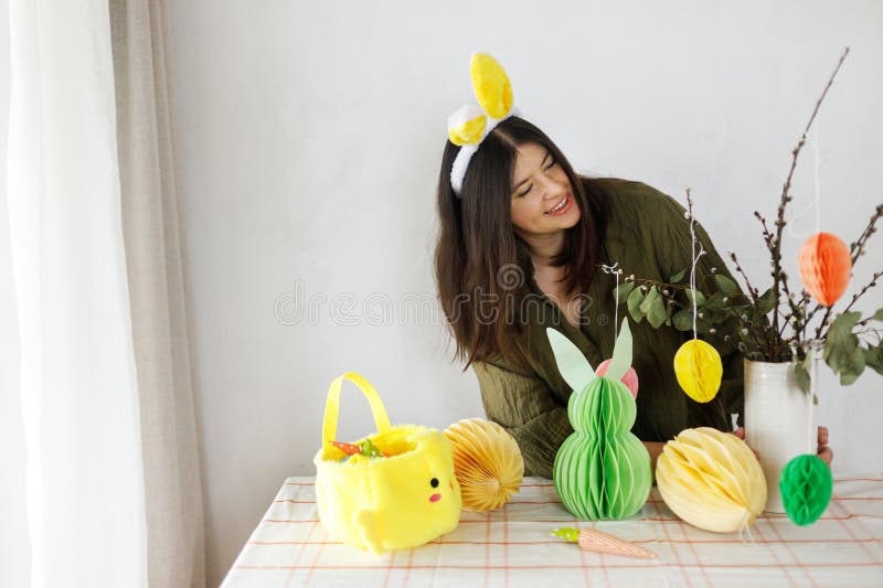 Joyeuse femme dans les oreilles de lapin décoré avec coloré vase d'oeufs en papier de pâques et carottes sur la table. Bonne Pâque images libres de droits