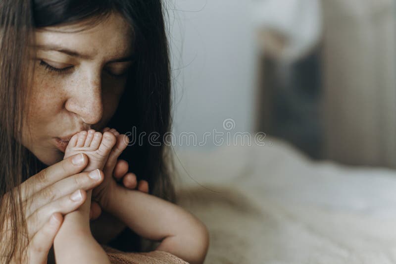 Joyeuse fête des mères! Mère embrasser les pieds de bébé nouveau-nés dans la chambre. Amour et concept familial. Maman tenant des photos libres de droits