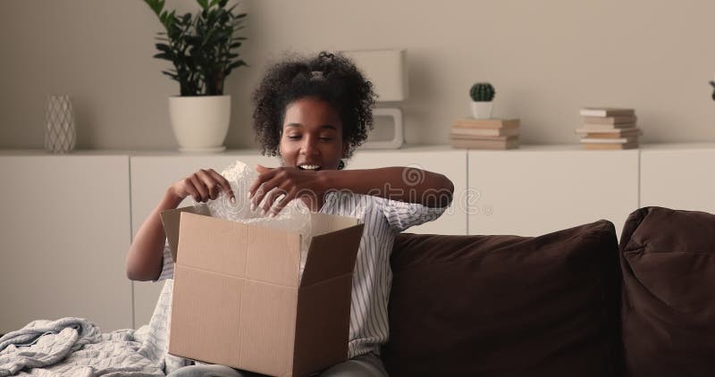 Joyeuse jeune africaine mixte race femme ouverture boîte en carton. clips vidéos