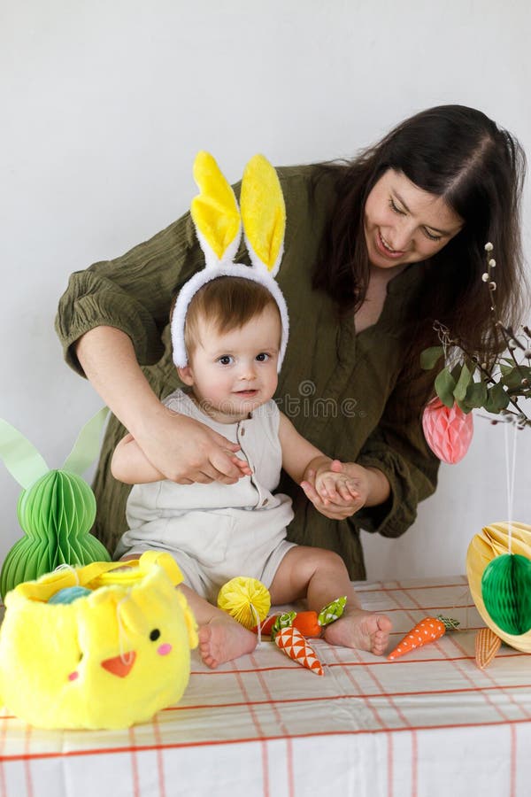 Joyeuse mère avec adorable bébé fils jouant et décorant avec des oeufs colorés de Pâques et des carottes du panier. Mignonne lapin photos libres de droits