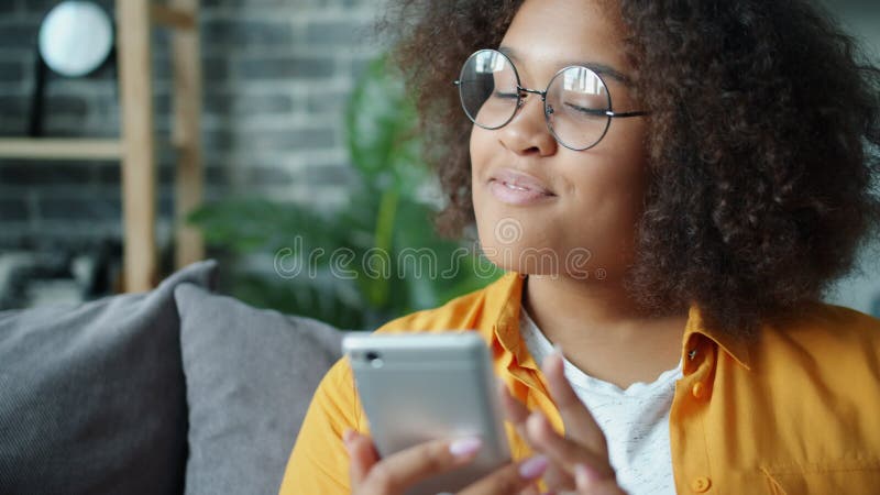 Joyeux adolescent afro-américain utilisant son smartphone à la maison riant banque de vidéos