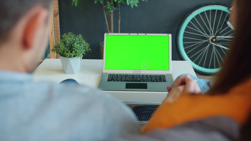 Joyeux couple regardant l'écran de clé chromatique vert pour ordinateur portable se tenant la main à la maison banque de vidéos