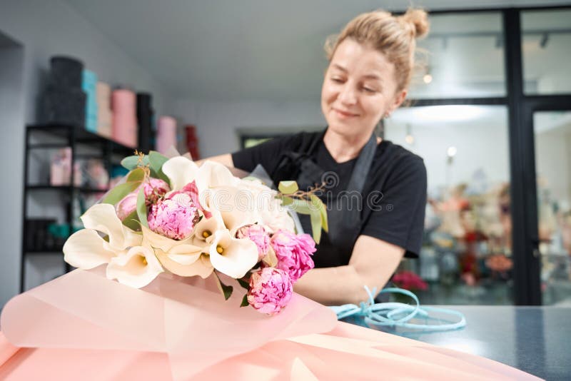 Joyeux fleuriste enveloppe le bouquet chic de fleurs dans le papier décoratif photographie stock