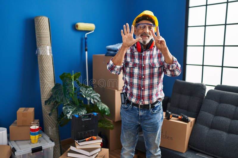 Joyeux homme senior en hardhat et lunettes de sécurité joyeusement montrer sept avec des doigts pointe vers le haut symbolique pou photos stock