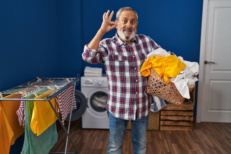 Joyeux homme senior en toute confiance gesturingoksign avec les doigts tient fièrement la corbeille de linge frais à l'intérieur image libre de droits