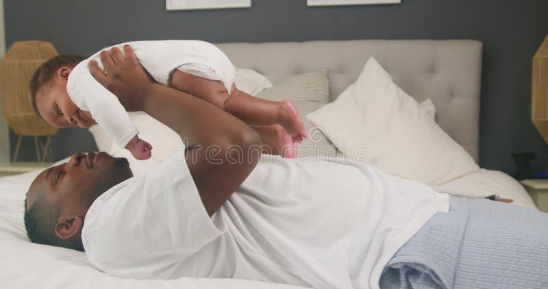 Joyeux père afro-américain et bébé jouant sur lit : Un moment d'amour et de connexion banque de vidéos
