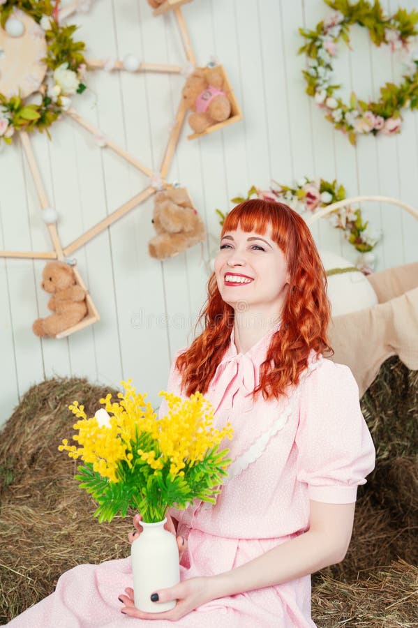 Joyeux rousse belle femme en robe rose tient un bouquet de printemps jaune vif dans un cadre rustique cosy photo stock