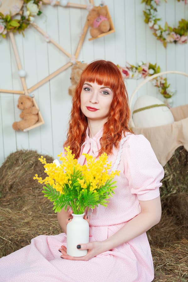 Joyeux rousse belle femme en robe rose tient un bouquet de printemps jaune vif dans un cadre rustique cosy photos stock