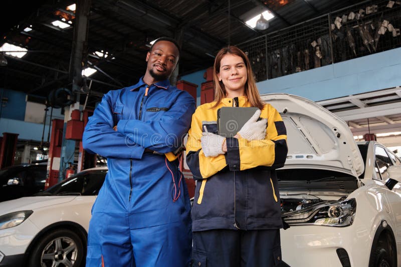 Joyeux travail d'équipe mécanique joyeux bras croisés avec le sourire dans garage de voiture fixe. image libre de droits
