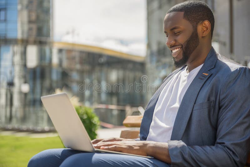 Joyful African man using computer outdoors