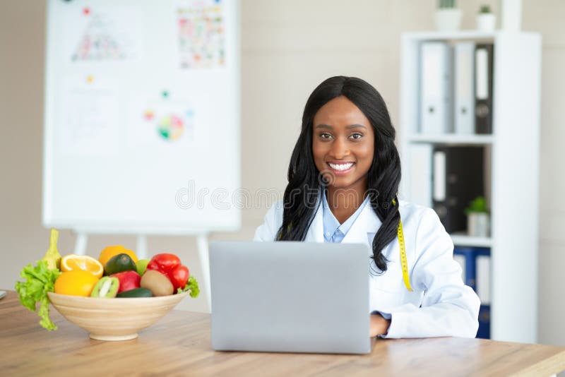 Joyful black female dietitian with laptop consulting patient online at clinic, empty space royalty free stock photos