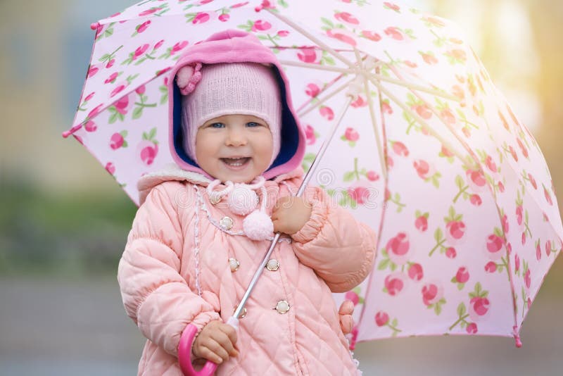 Bambino gioioso con fiore rosa ombrello alla luce del sole dopo la pioggia.