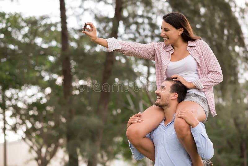 Pretty young women sitting on the shoulders of her boyfriend and taking sel...