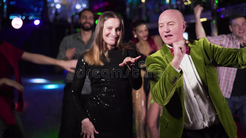 Joyful elderly Caucasian man and young woman dancing in night club. Positive people of different ages resting in the