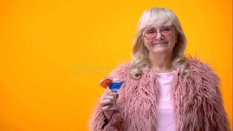 Joyful elderly woman holding blue cocktail, smiling into camera, party mood stock photos Joyful elderly woman holding blue cocktail, smiling into camera, party mood stock photos