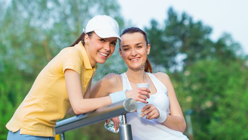Joyful girlfriends in sports clothing drinking water