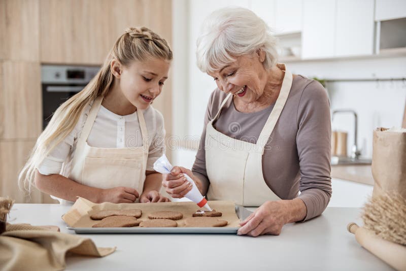 Cheerful girl baking holiday sweet food with granny stock photos Cheerful girl baking holiday sweet food with granny stock photos