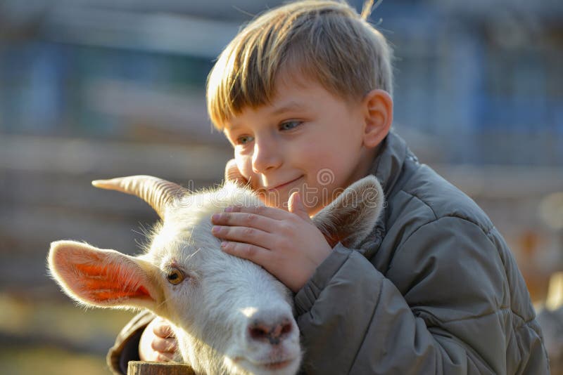 Joyful and happy boy hugs and strokes a horned goat, the concept of the unity of nature and man