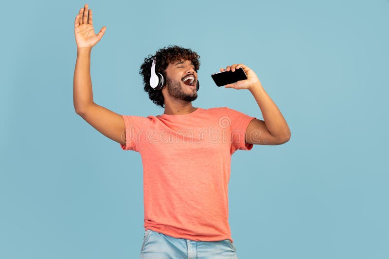 Joyful Indian Guy Singing Karaoke, Using Smartphone and Headset Stock
