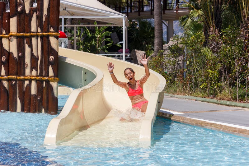 Joyful laughing teen girl goes down by water slide in the hotel aquapark