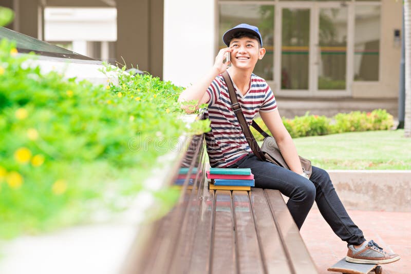 Joyful male student sitting on the bench and talking on the phone