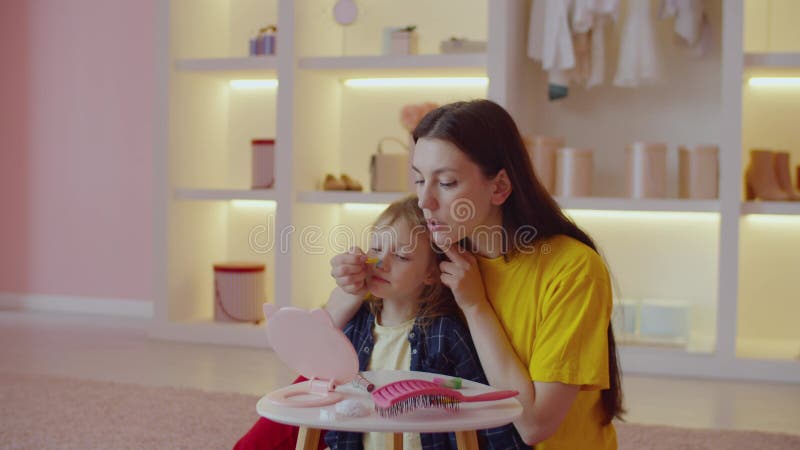 Joyful pretty mother and cute little daughter making festive makeup at home