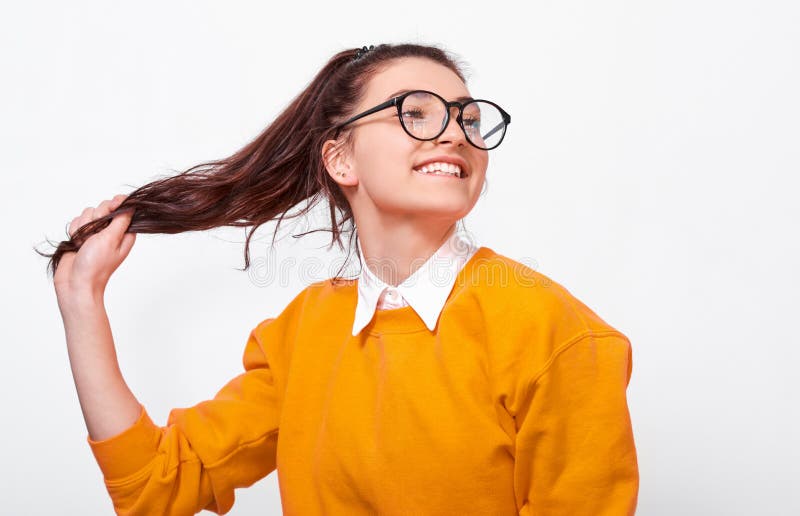 Joyful Teenager Girl, lächelnd breit, berührend ponytail, mit orangefarbenem Pullover und rundum transparenten Brillen Hübsches W lizenzfreies stockfoto Joyful Teenager Girl, lächelnd breit, berührend ponytail, mit orangefarbenem Pullover und rundum transparenten Brillen Hübsches W lizenzfreies stockfoto