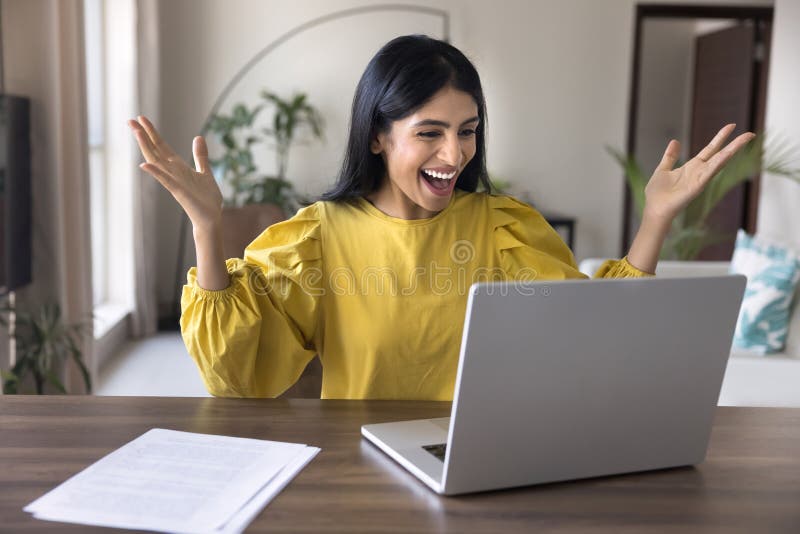 Joyful, ung indiansk kvinna som njuter av att vinna på en bärbar dator fotografering för bildbyråer