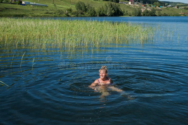 A joyful woman is floating in the lake, against the backdrop of the village. royalty free stock image A joyful woman is floating in the lake, against the backdrop of the village. royalty free stock image