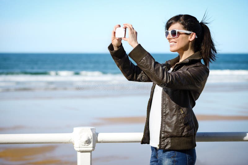 Joyful woman taking photo with cell phone on the beach on spring. Happy girl on vacation taking picture on sea background. Joyful woman taking photo with cell phone on the beach on spring. Happy girl on vacation taking picture on sea background.