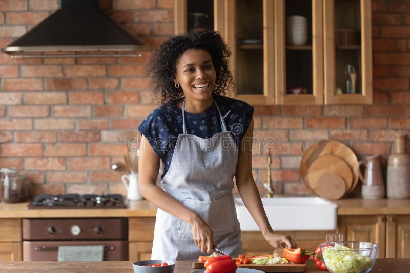 Joyful young afro american lady cut vegetable salad for lunch