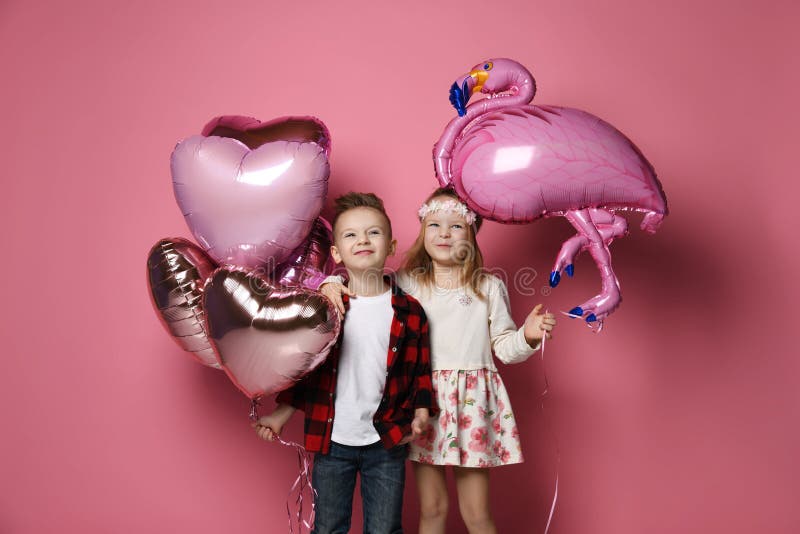 Joyfull Little boy with color heart balloons and nice little girl with flamingo balloon came together at the party