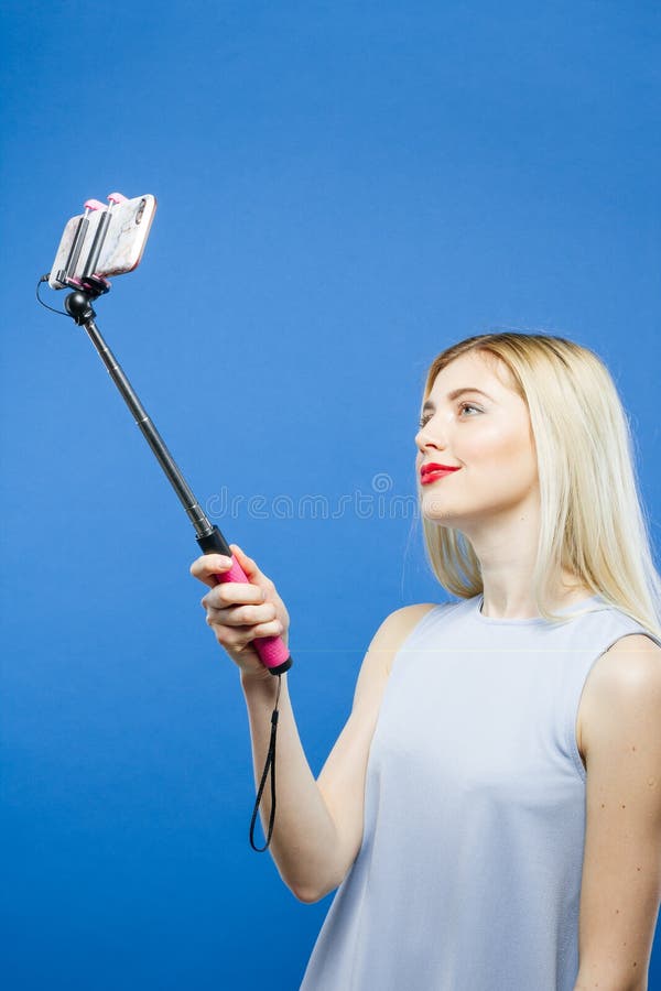 Joyous Blonde die Foto nemen die Selfie-Stok op Blauwe Achtergrond gebruiken Leuk Meisje in Kleding die fotograferen door Smartph stock afbeelding Joyous Blonde die Foto nemen die Selfie-Stok op Blauwe Achtergrond gebruiken Leuk Meisje in Kleding die fotograferen door Smartph stock afbeelding