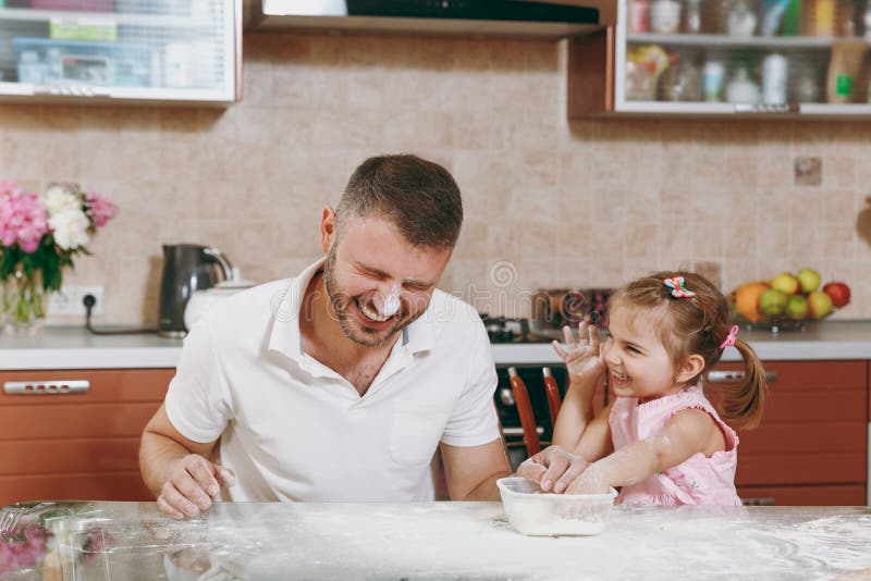 Little kid girl play with men smearing dad with flour in kitchen at table. Happy family dad, child daughter cooking food cookies in weekend morning at home. Father`s day holiday. Parenthood childhood. Little kid girl play with men smearing dad with flour in kitchen at table. Happy family dad, child daughter cooking food cookies in weekend morning at home. Father`s day holiday. Parenthood childhood