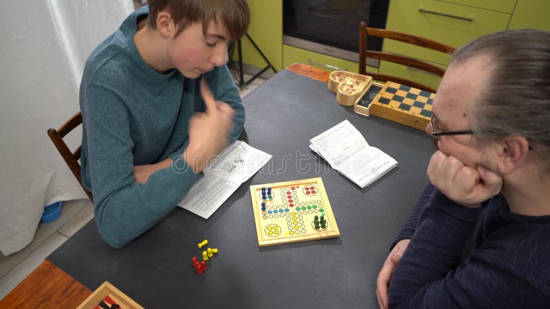 Juego de mesa Ludo. Adolescente y papá juegan en casa. Manos de los jugadores. Tiempo de familia metrajes