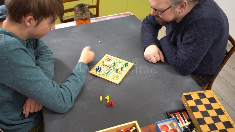 Juego de mesa Ludo. Adolescente y papá juegan en casa. Manos de los jugadores. Tiempo de familia metrajes