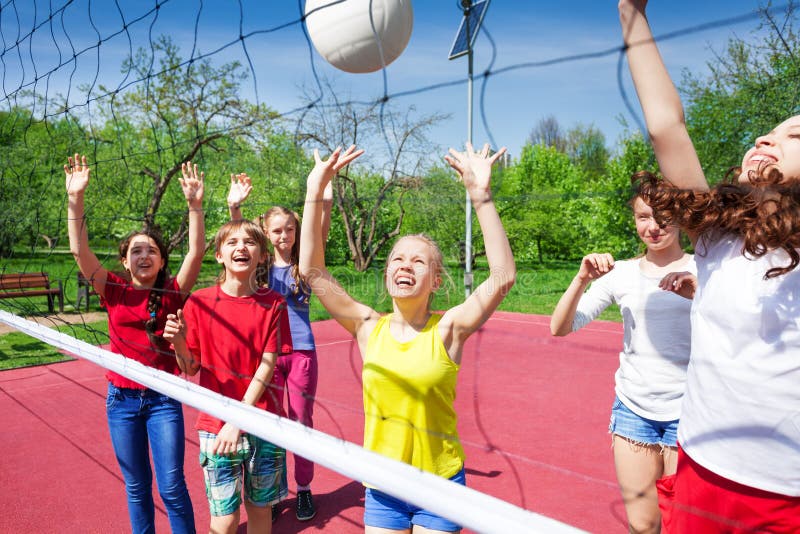 Children play actively near the volleyball net on the court during sunny summer day outside. Children play actively near the volleyball net on the court during sunny summer day outside