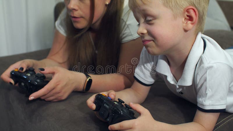 Juegos de ordenador del juego de la madre y del hijo con las palancas de mando que mienten en el sofá almacen de metraje de vídeo