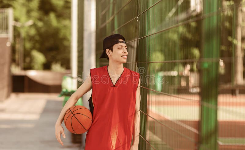 Jugador de baloncesto de Asia del Milenio con balón parado cerca de la valla en el estadio deportivo al aire libre fotos de archivo