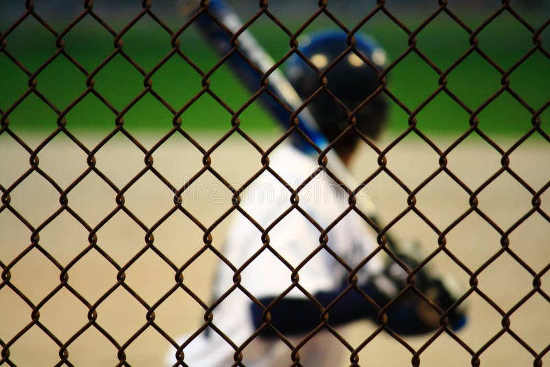 A teenage baseball player readies for a pitch from this abstract view of baseball behind the chain link fence. A teenage baseball player readies for a pitch from this abstract view of baseball behind the chain link fence.