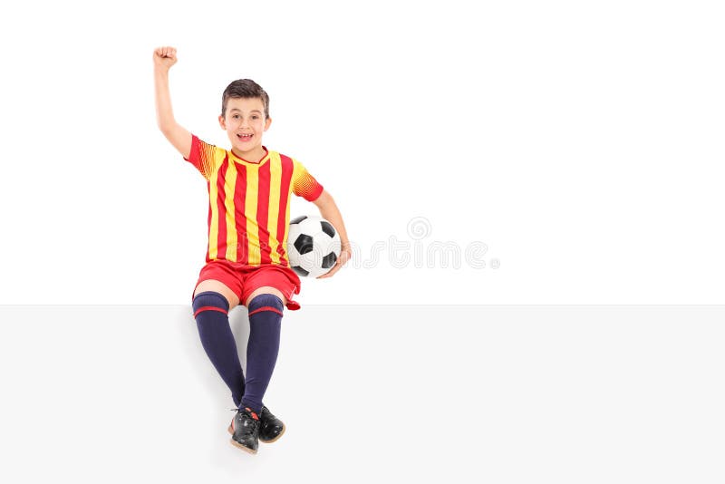 Jugador de fútbol menor que gesticula la alegría asentada en el panel fotos de archivo Jugador de fútbol menor que gesticula la alegría asentada en el panel fotos de archivo