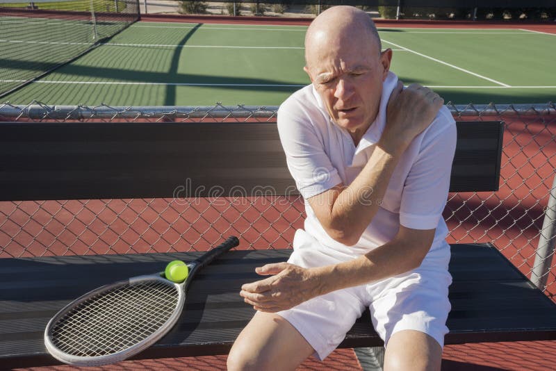Jugador de tenis de sexo masculino mayor con el dolor del hombro que se sienta en banco en la corte