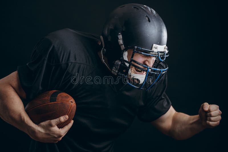 Jugador del deportista del fútbol americano en la acción aislado sobre la pared negra del estudio imagen de archivo Jugador del deportista del fútbol americano en la acción aislado sobre la pared negra del estudio imagen de archivo