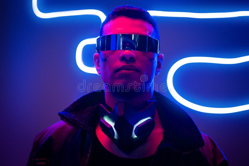 Mixed race cyberpunk player in futuristic glasses near blue neon lighting. Mixed race cyberpunk player in futuristic glasses near blue neon lighting